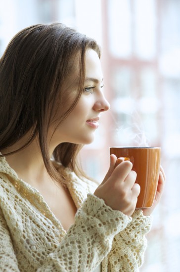 Beautiful young girl drinking hot tea while looking at the window