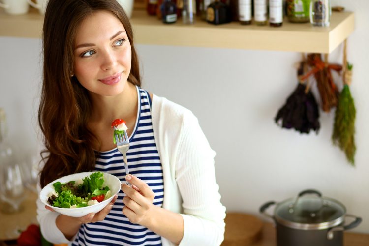 Young woman eating salad and holding a mixed salad .