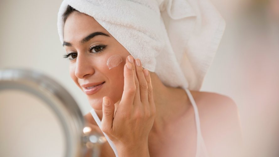 Woman with hair in towel rubbing lotion on face